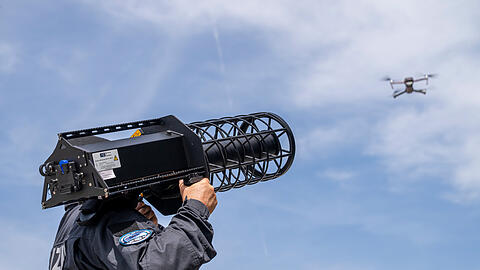 Ein Polizist steht w&auml;hrend einer Demonstration im Rahmen der Er&ouml;ffnung des Drohnenkompetenz- und -abwehrzentrum mit einem "Counter LAV Jammer HP 47 + PR V7" hinter einer Drohne. Damit l&auml;sst sich eine Drohne vom Himmel holen. Das 2025 beschlossene Drohnenkompetenz- und -abwehrzentrums (DKAZ) ist eine direkte Reaktion auf die steigende Zahl an Vorf&auml;llen mit Drohnen in Bayern, etwa &uuml;ber Flugh&auml;fen.