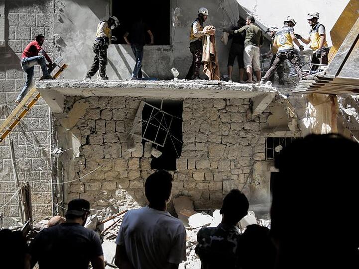 Menschen stehen vor einem Gebäude, das bei einem Luftangriff am 27. Mai durch die syrischen Regierungskräfte beschädigt wurde.