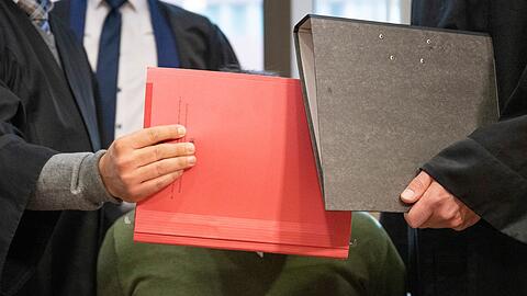 Mit Aktenmappen schirmen die Anwälte den Angeklagten im Verhandlungssaal des Landgerichts in Frankfurt ab.
