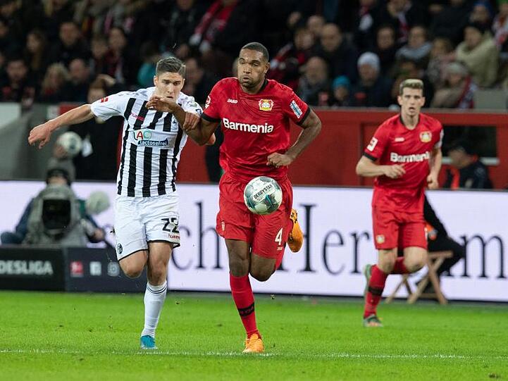 Leverkusens Jonathan Tah (M) und Freiburgs Roland Sallai kämpfen um den Ball.