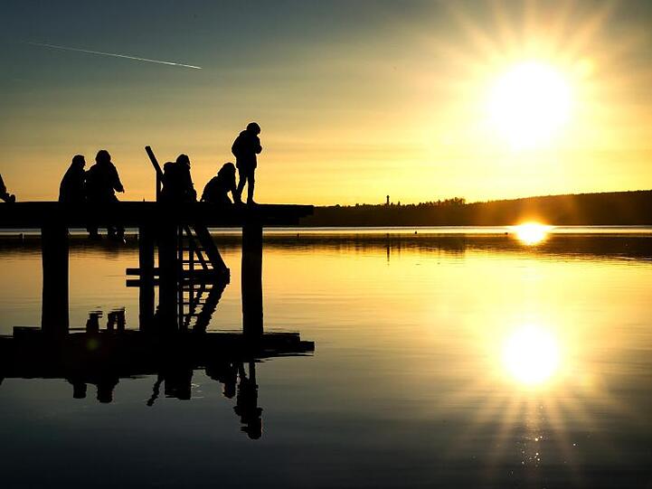 Auf einem Steg über dem Ammersee sitzend, beobachten Ausflügler den Sonnenuntergang. Foto: Sina Schuldt