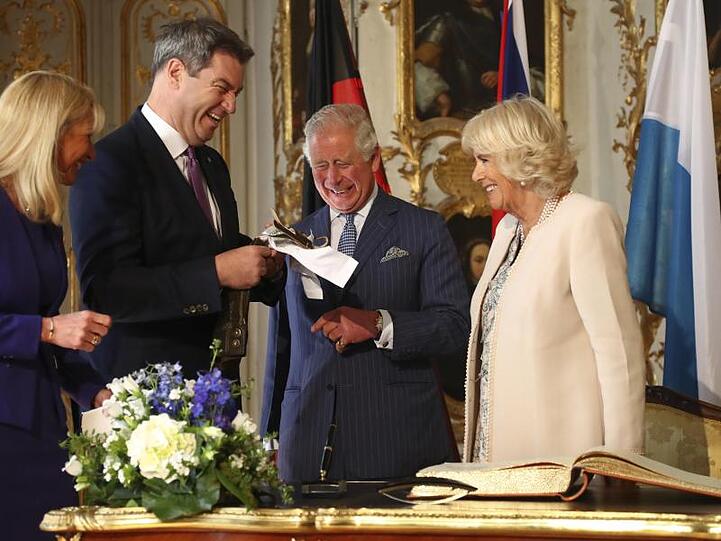 Ministerpräsident Markus Söder (CSU, 2.v.l) überreicht Prinz Charles und seiner Frau, Herzogin Camilla, eine Mini-Lederhose. Für Archie Harrison.