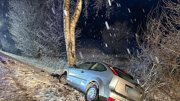 Ein Auto landet bei schneeglatter Fahrbahn an einem Baum.