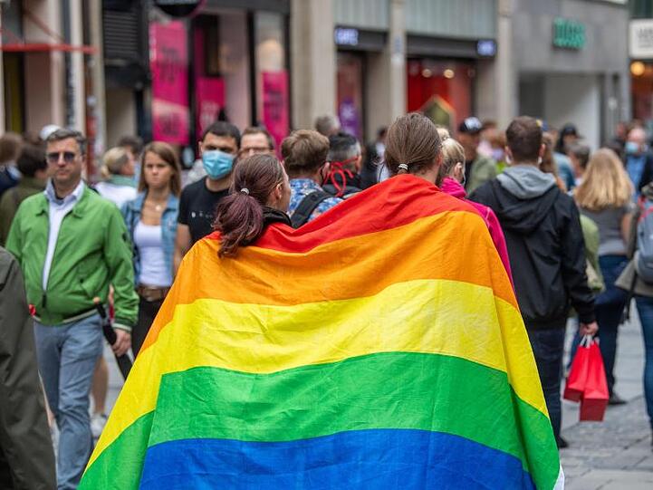 Zwei Frauen laufen umhüllt von einer Pride-Flagge durch die Münchner Innenstadt.