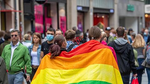 Zwei Frauen laufen umhüllt von einer Pride-Flagge durch die Münchner Innenstadt.