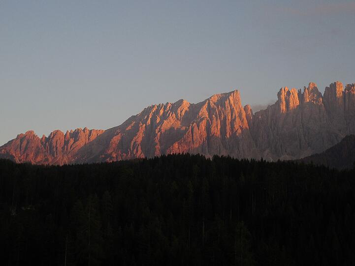 Alpenglühen: Die untergehende Sonne verwandelt die Felswand des Latemar in orange flackernde Flammen.