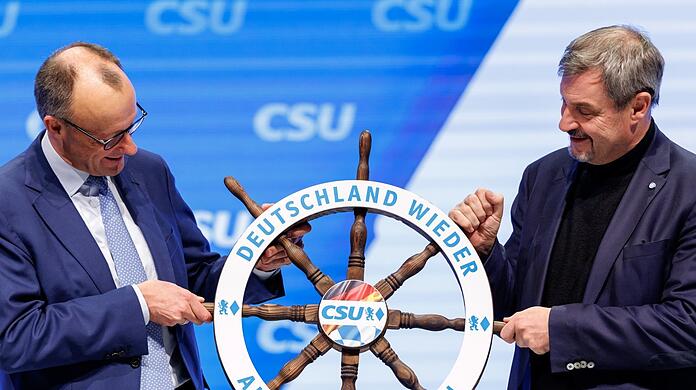 Eine Erwartung als Geschenk: Markus Söder (r.) übergibt an Friedrich Merz ein Steuerrad mit der Aufschrift "Deutschland wieder auf Kurs bringen".