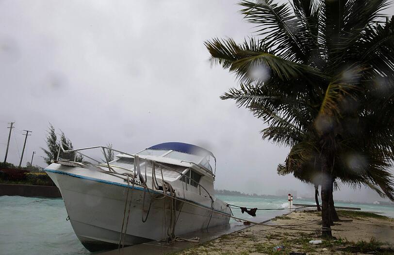 Wind und Regen haben diese kleine Jacht auf den Bahamas an die Steinmauer im Hafen geschleudert. Das kaputte Heck des Schiffes sinkt bereits, der Rest treibt hilflos auf dem Wasser.