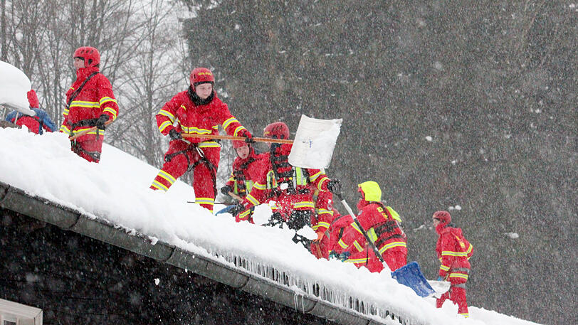 Helfer der Deutschen Lebens-Rettungs-Gesellschaft (DLRG) räumen im Landkreis Traunstein Schnee von einem Hausdach.