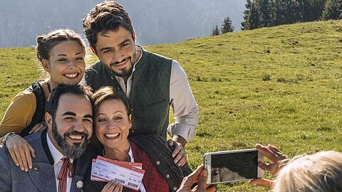"Servus, Schwiegersohn!": Toni (Adnan Maral, sitzend) lässt sich mit Ehefrau Anne (Jule Ronstedt), Tochter Franzi (Lena Meckel, stehend) und Schwiegersohn Osman (Aram Arami) ablichten.