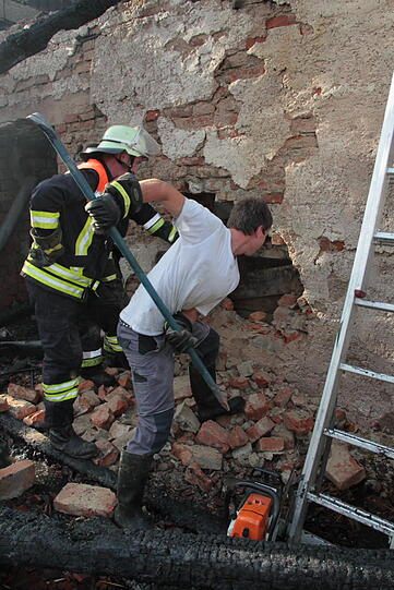 Hinter einer eingestürzten Mauer im abgebrannten Bauernhof ist noch ein Kuhkalb eingesperrt. Mit bloßer Hand und einem Geißbein durchbrechen die Feuerwehrleute eine 50 Zentimeter dicke Mauer und retten es.