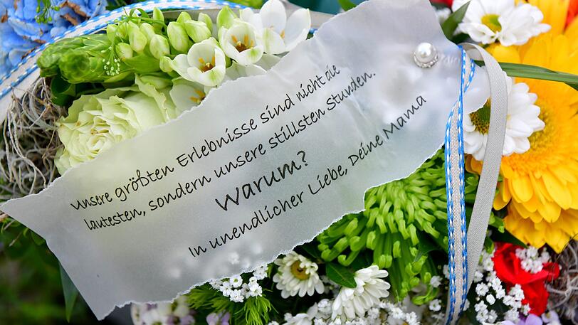 Blumengebinde von Angehörigen liegen an einer noch unbeschrifteten Grabsäule auf dem Friedhof.