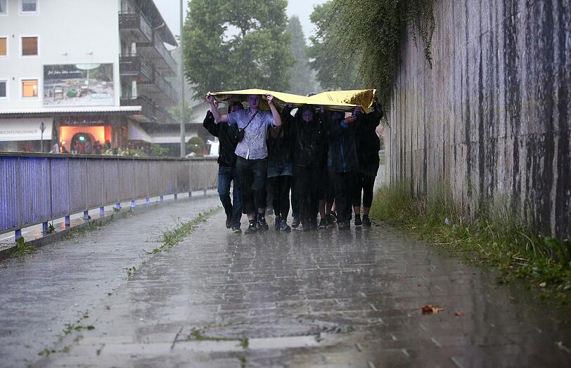 Mit einer Folie versuchen sich Menschen in Garmisch vor dem Regen zu schützen.