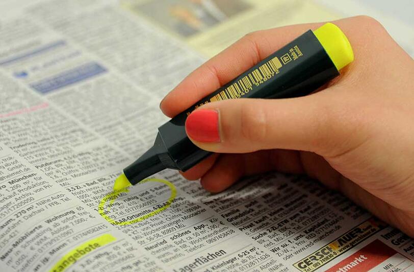 Eine Frau markiert im Immobilienteil einer Zeitung in München mit einem Textmarker eine Wohnungsanzeige.