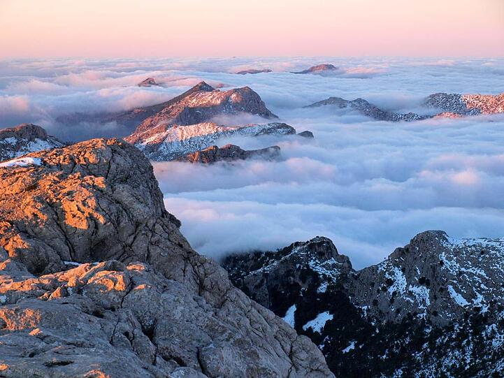 Einen malerischen Anblick bieten die in ein Wolkenmeer gehüllten Berggipfel am Puig de l'Ofre.