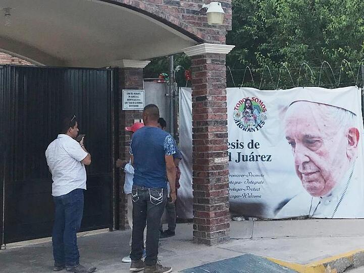 Hinter einem Zaun der Migrantenherberge Casa del Migrante, an dem ein großes Abbild von Papst Franziskus hängt, stehen einige Bewohner der Herberge.