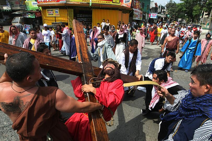 Ein Jesus-Darsteller trägt mit Dornenkrone ein riesiges Holz-Kreuz.