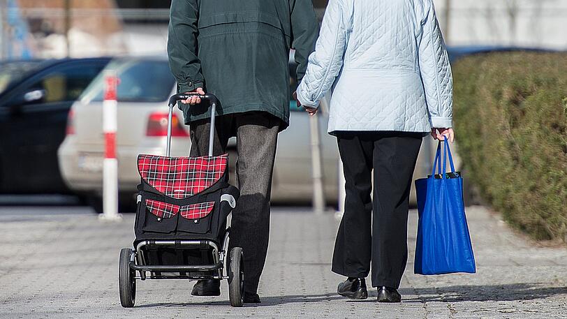 Ein älteres Paar geht mit Einkaufstrolley und -tasche durch die Straßen. (Symbolbild)