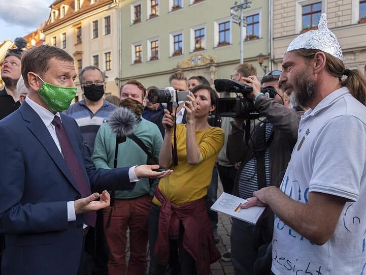 Sachsens Ministerpräsident Michael Kretschmer (l) spricht in Pirna mit einem Gegner der Corona-Maßnahmen.