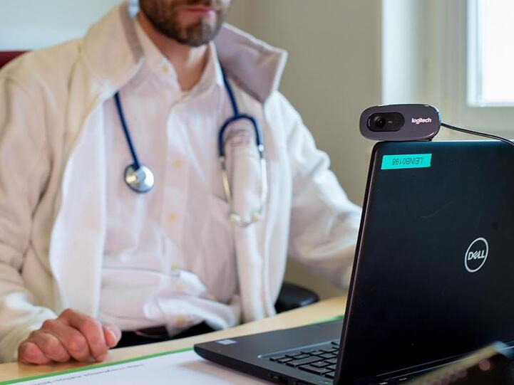 Ein Hausarzt spricht während einer Videosprechstunde in seiner Praxis mit einer Patientin.