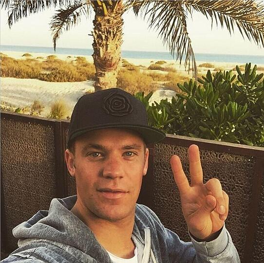 Manuel Neuer grüßt vor malerischer Palmen-und-Strand-Kulisse.