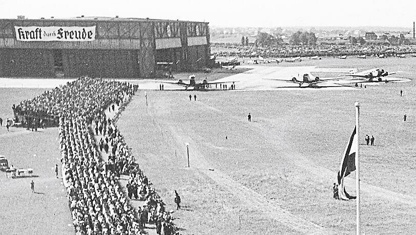 "Kraft durch Freude" steht auf dem Plakat hinten bei einem "Großflugtag" auf dem Oberwiesenfeld 1935. "Kraft durch Freude" steht auf dem Plakat hinten bei einem "Großflugtag" auf dem Oberwiesenfeld 1935.