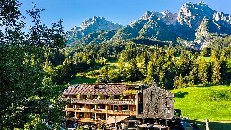 Was f&uuml;r eine Kulisse! Das mama thresl vor den Leoganger Steinbergen &ndash; mit Kletterwand an der Fassade.