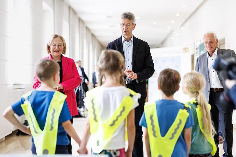 Irmgard Stippler, Vorstandsvorsitzende der AOK Bayern (v.l.), und Kultusminister Michael Piazolo (Freie Wähler) haben den Kindern in der St.-Anna-Grundschule Warnwesten mitgebracht.