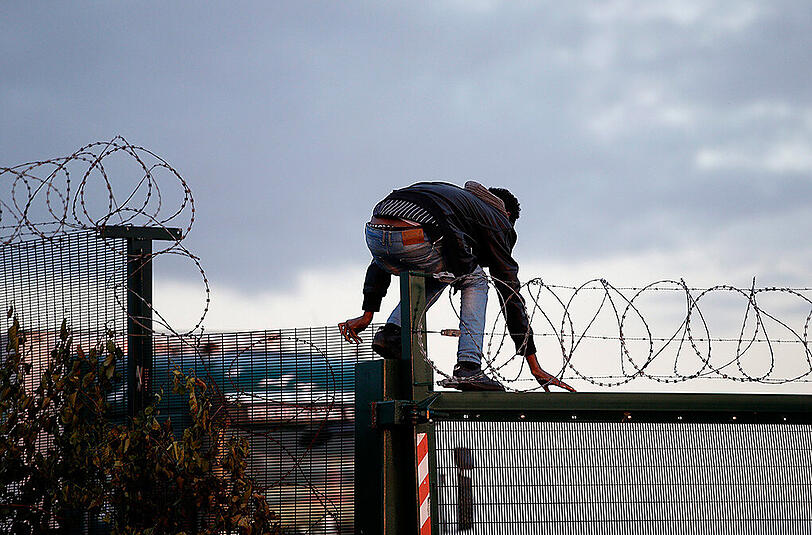 In Calais klettert ein Flüchtling über einen Zaun, um zum Eurotunnel-Terminal zu gelangen.