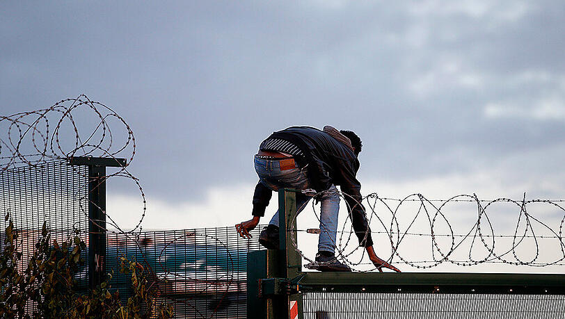In Calais klettert ein Flüchtling über einen Zaun, um zum Eurotunnel-Terminal zu gelangen.
