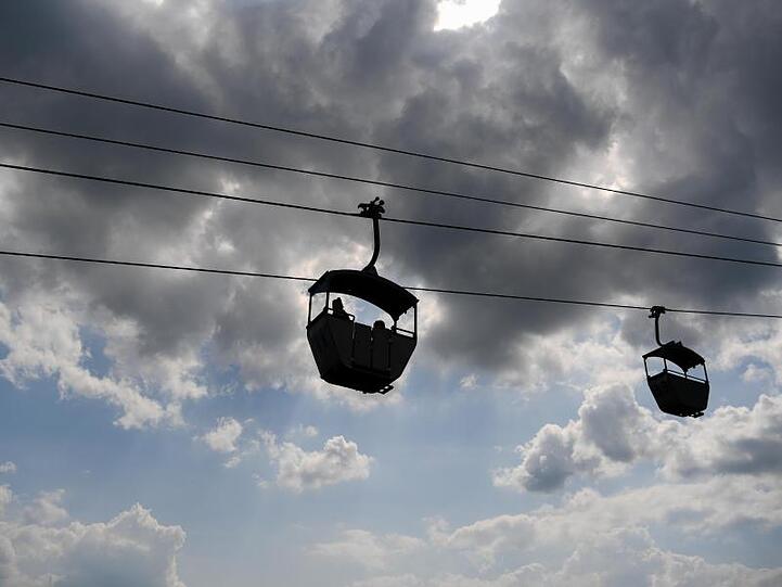 Zwei Gondeln einer Seilbahn sind am Himmel zu sehen. Foto: Arne Dedert/Archivbild