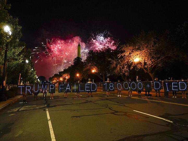 Demonstranten halten Schilder auf denen Leuchtdioden eine Botschaft bilden, während ein Feuerwerk den Himmel um das Washington Monument erhellt, welches zum Abschluss des Parteitages der Republikaner gezündet wird.
