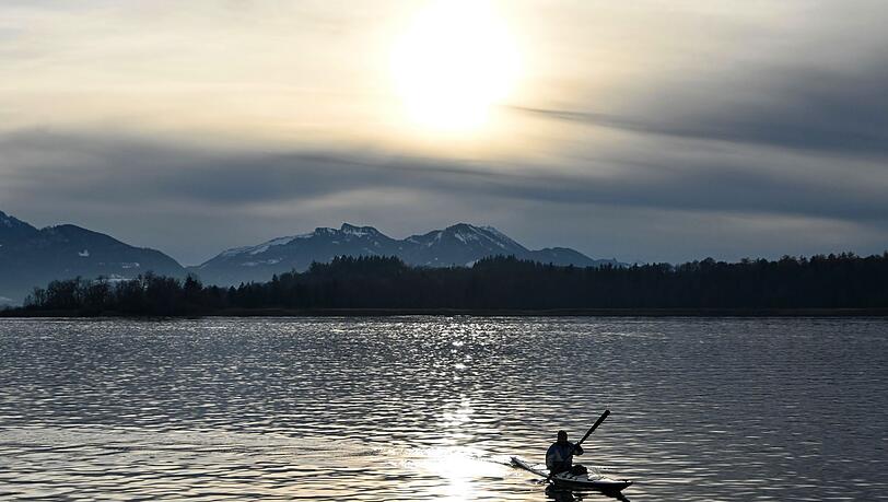Ein Kajakfahrer fährt vor schneebedeckten Bergen über den Chiemsee.