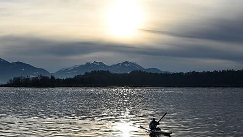 Ein Kajakfahrer fährt vor schneebedeckten Bergen über den Chiemsee.
