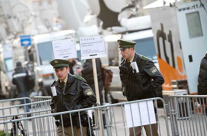 Zwei Polizisten laufen vor Übertragungswagen von verschiedenen Fernsehsendern vorbei.