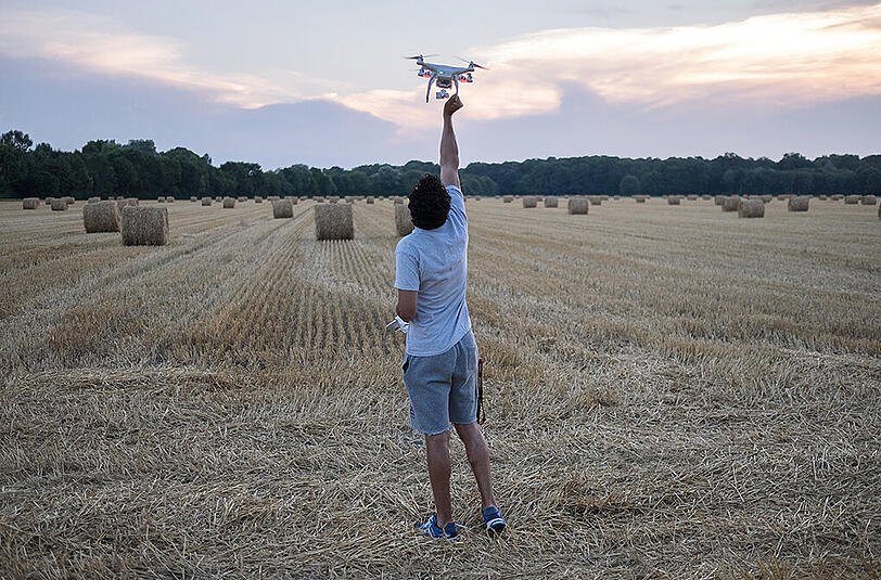 Aus der Ausstellung &bdquo;Freiraum 2030&ldquo;: Ein junger Mann spielt mit einem Quadrocopter auf einer Feldflur im Münchner Norden.