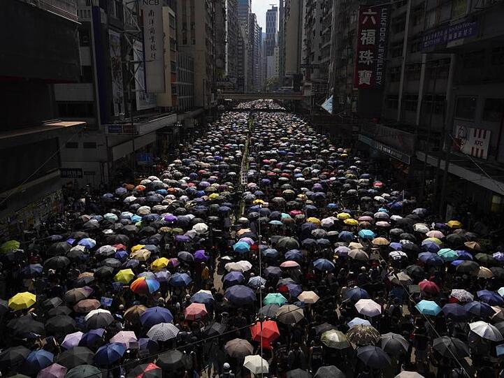 Tausende Hongkonger ziehen mit Regenschirmen über eine Straße.