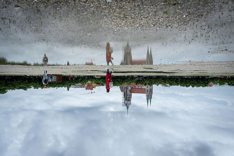 Die Paulskirche am Rand der Theresienwiese spiegelt sich in einer Pfütze auf einer der Straßen zwischen den Flächen mit Kies und Magerrasen.