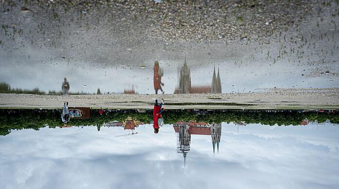 Die Paulskirche am Rand der Theresienwiese spiegelt sich in einer Pfütze auf einer der Straßen zwischen den Flächen mit Kies und Magerrasen.