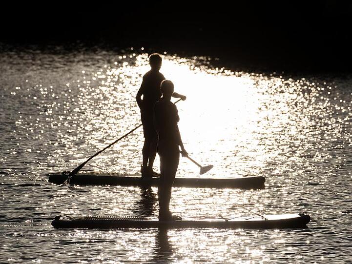 Stehpaddler (Stand Up Paddling) gleiten in der Abendsonne über einen See.