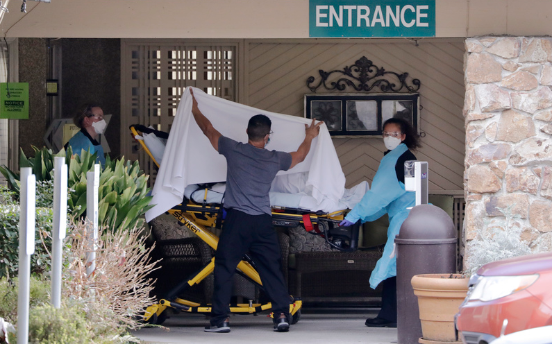 USA, Kirkland: Ein Mitarbeiter verdeckt eine Person, die auf einer Bahre zu einem wartenden Krankenwagen vor einer Pflegeeinrichtung gebracht wird. Nach Bekanntwerden des ersten Toten durch das neuartige Coronavirus im Land haben die USA davon abgeraten, in die betroffenen Regionen in Italien und Südkorea zu reisen.