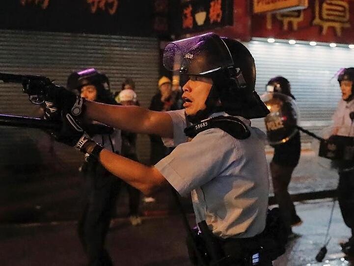 Ein Polizist zielt mit seiner Waffe auf Demonstranten.