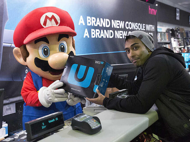 Ein Mario-Maskottchen händigt einem Kunden die derzeit noch aktuelle Nintendo-Heimkonsole Wii U aus
