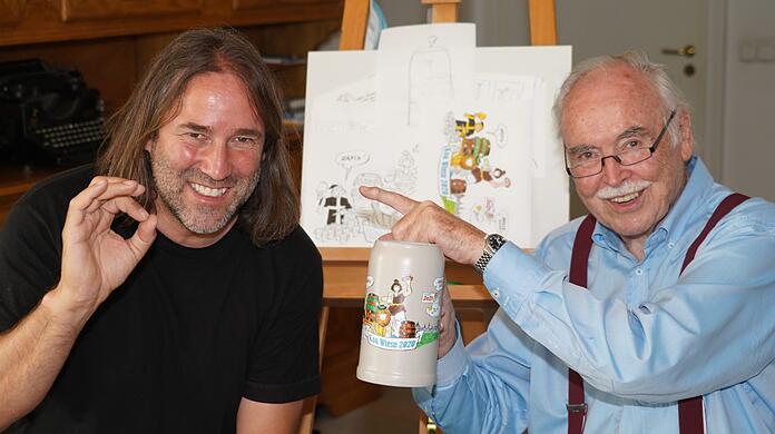Liedermacher Roland Hefter (links) daheim bei AZ-Karikaturist Dieter Hanitzsch, der den Koa-Wiesn-Krug 2020 bemalt hat, aber den Fingerzeig gibt: Die Idee dazu hatte der umtriebige Sänger.