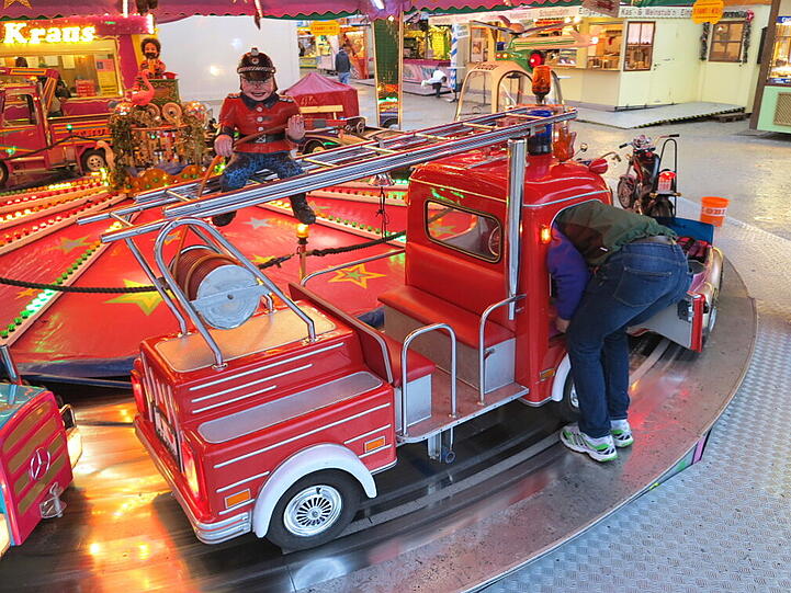 Ein Mann putzt das Feuerwehrauto am Karussell.