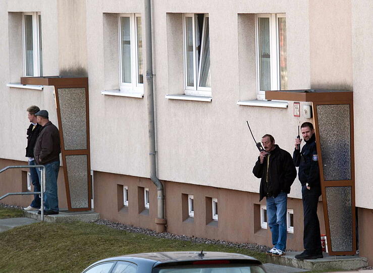 Polizisten stehen am Dienstag vor einem Haus in Bad Langensalza, in dem sich ein Mann mit seinem Sohn verschanzt hat, während Nachbarn die Szenerie vom Fenster aus verfolgen.