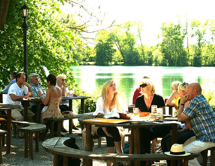 Und grünlich schimmert der See: Direkt am Wasser vom Langwieder sitzen die Gäste im Biergarten am Langwieder See.