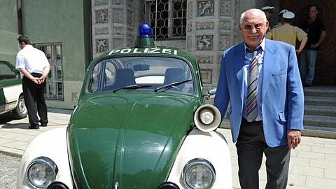 Rolf Schimpf steht 2013 vor dem Polizeipräsidium in München neben einem alten VW-Käfer-Polizeiauto. Foto: Andreas Gebert/dpa/Archivbild