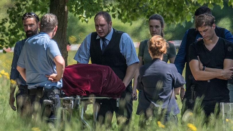 Auf einer Bahre transportieren Bestatter die Leiche einer jungen Frau ab. Um sie herum stehen Mitarbeiter der Polizei und der Gerichtsmedizin. Nach ersten Erkenntnissen der Polizei ist die bislang nicht identifizierte Frau Opfer eines Gewaltverbrechens geworden. Spaziergänger hatten den leblosen Körper am Morgen am Rande eines Parks gefunden.