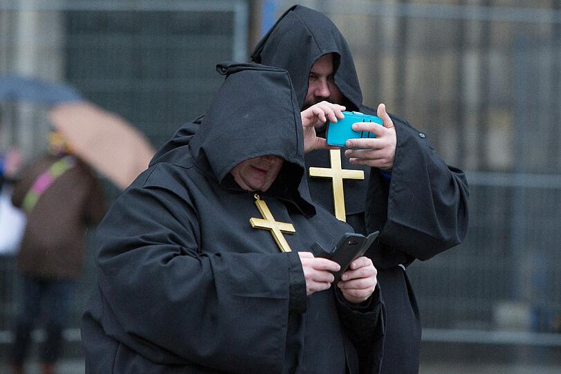Zwei als Mönche verkleidete Karnevalisten schauen am Rosenmontag in Köln auf ihre Handys.